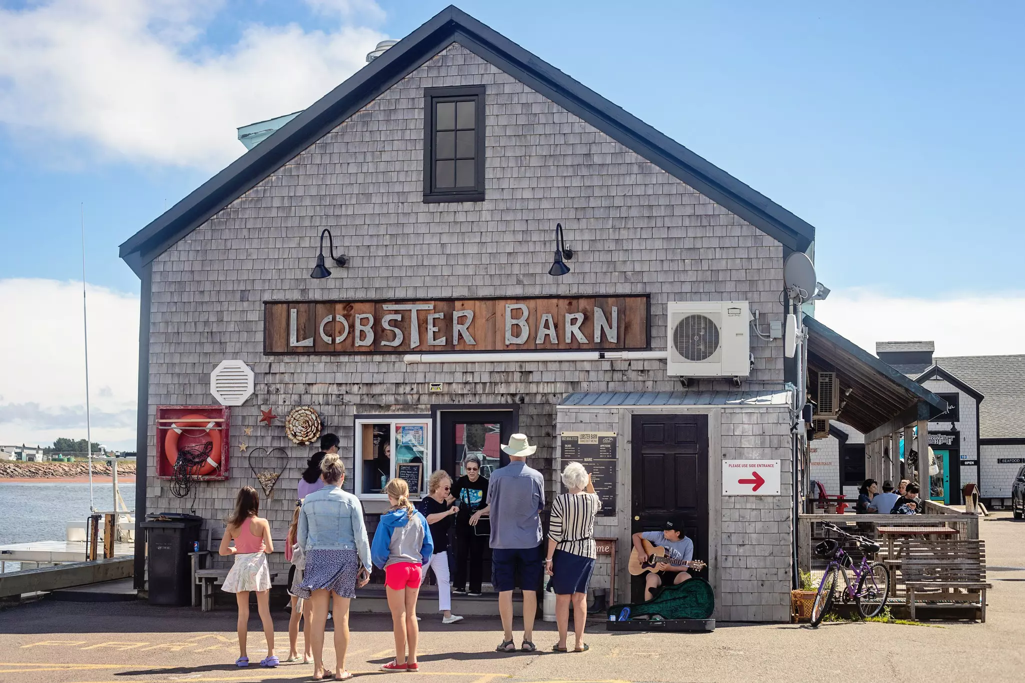 A line-up forms alongside a busker outside of the Lobster Barn, one of the top-rated eateries in Victoria by the Sea, Prince Edward Island.