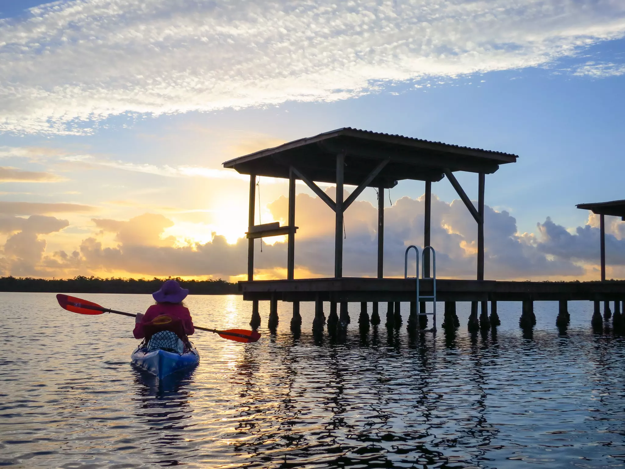A kayaker approaches a wooden above-water platform as the sun sets.