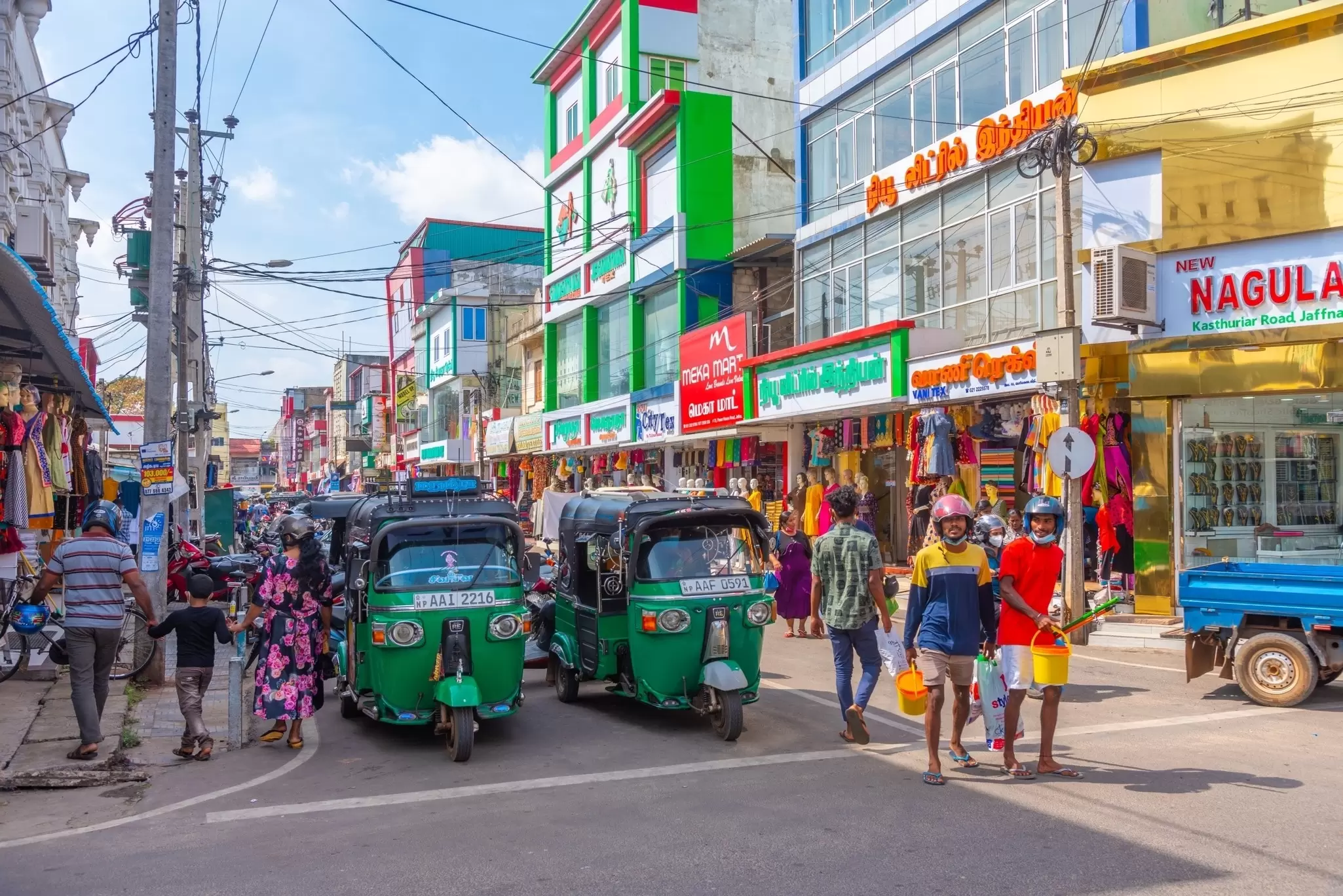 Colorful buildings lining a busy street filled with people and green tuk tuks.