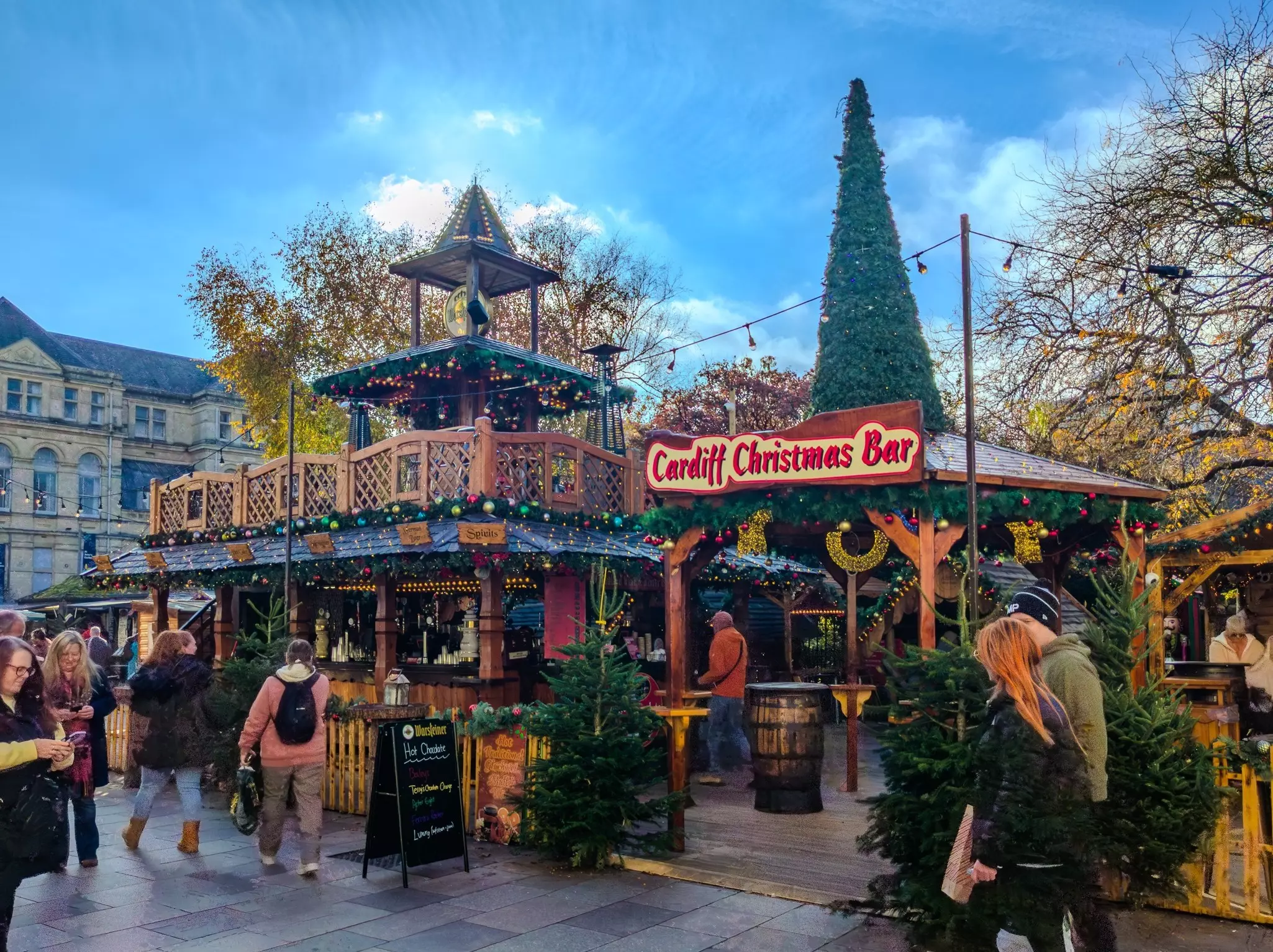 People walking around an outdoor Christmas market with booths that are decorated with ornaments