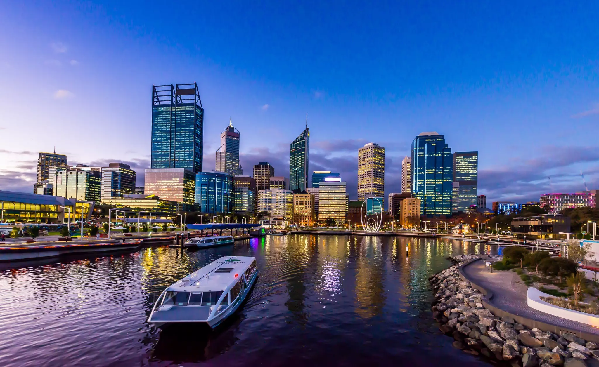 A ferry in a city dock at twilight with high-rise buildings behind.