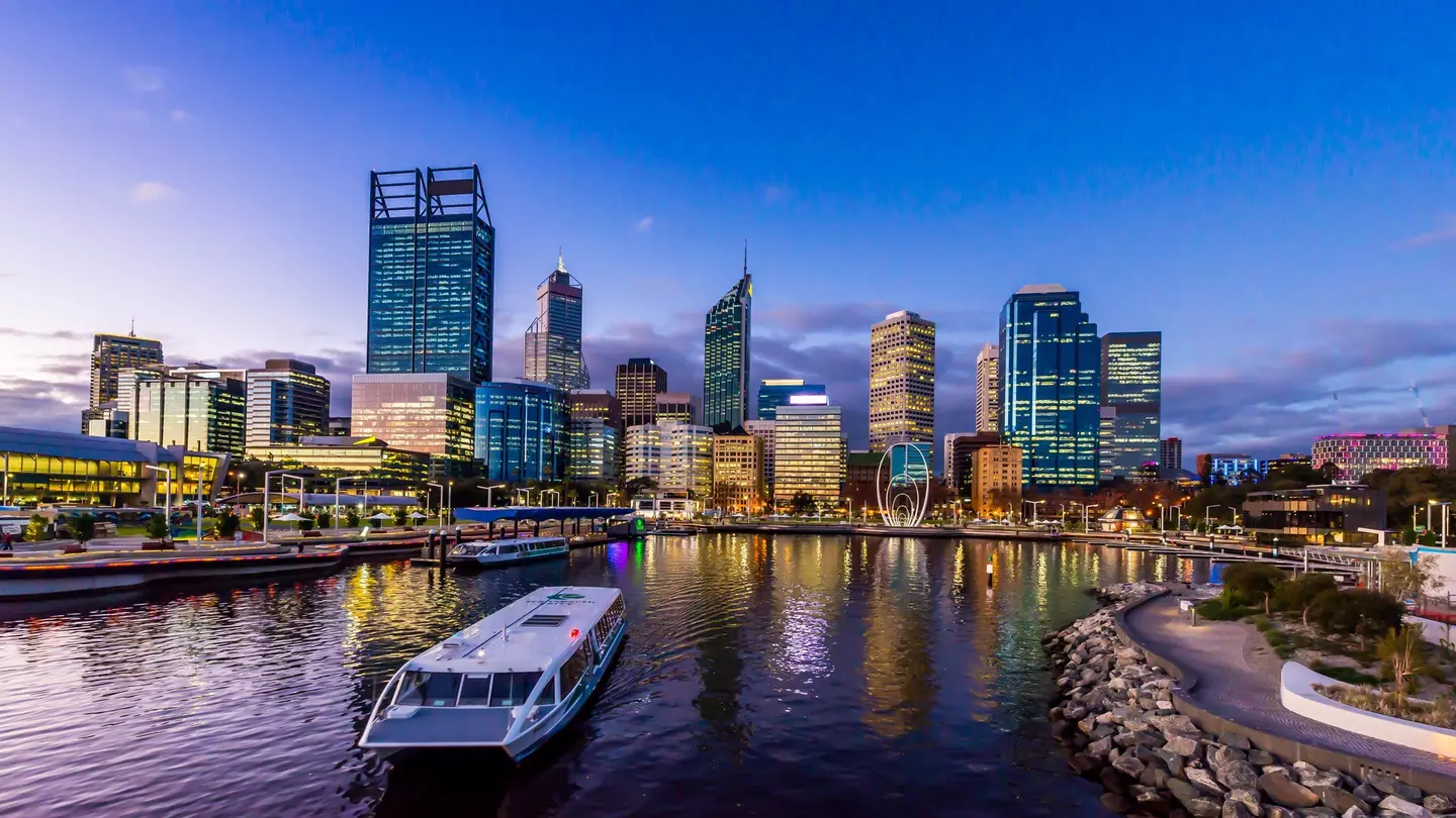 A ferry in a city dock at twilight with high-rise buildings behind.