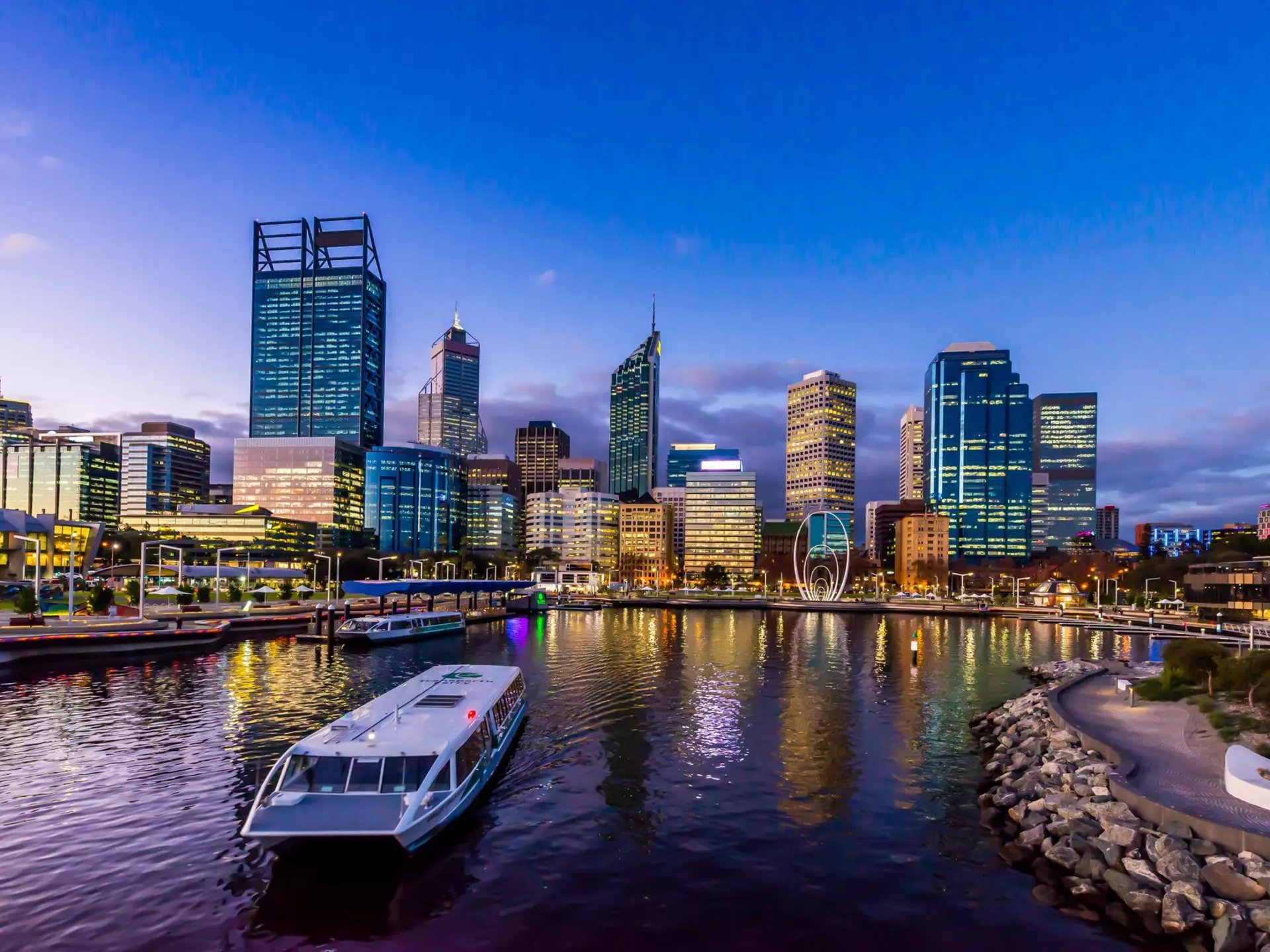 A ferry in a city dock at twilight with high-rise buildings behind.