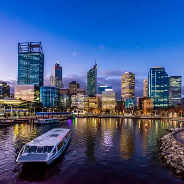 A ferry in a city dock at twilight with high-rise buildings behind.