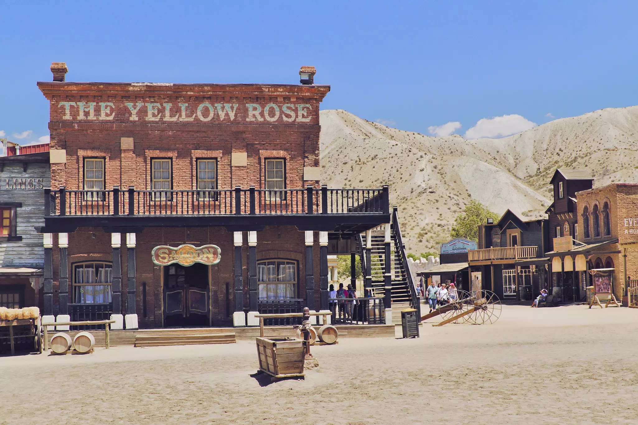 Tourists wander around a Wild West-style dust-filled street near a large wooden-fronted saloon.