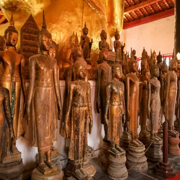 Rows of gilded wooden standing Buddha statues on a red floor inside the sim of Wat Wisunarat in Luang Prabang