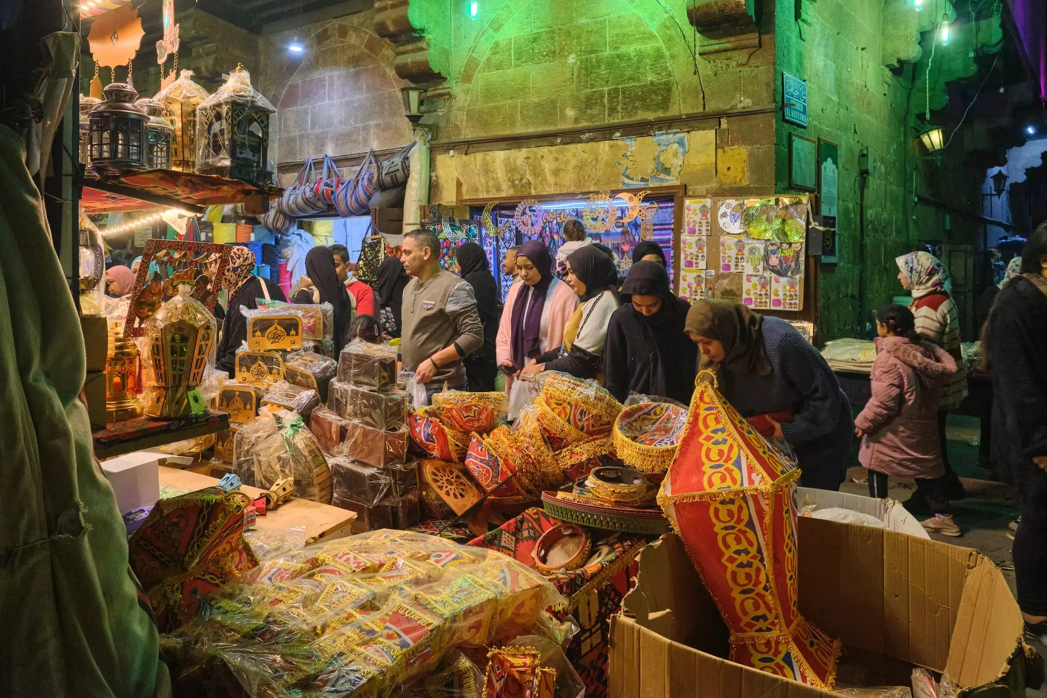 People shop in the evening at a well-lit street market with vendors selling lamps, baskets and other decor.