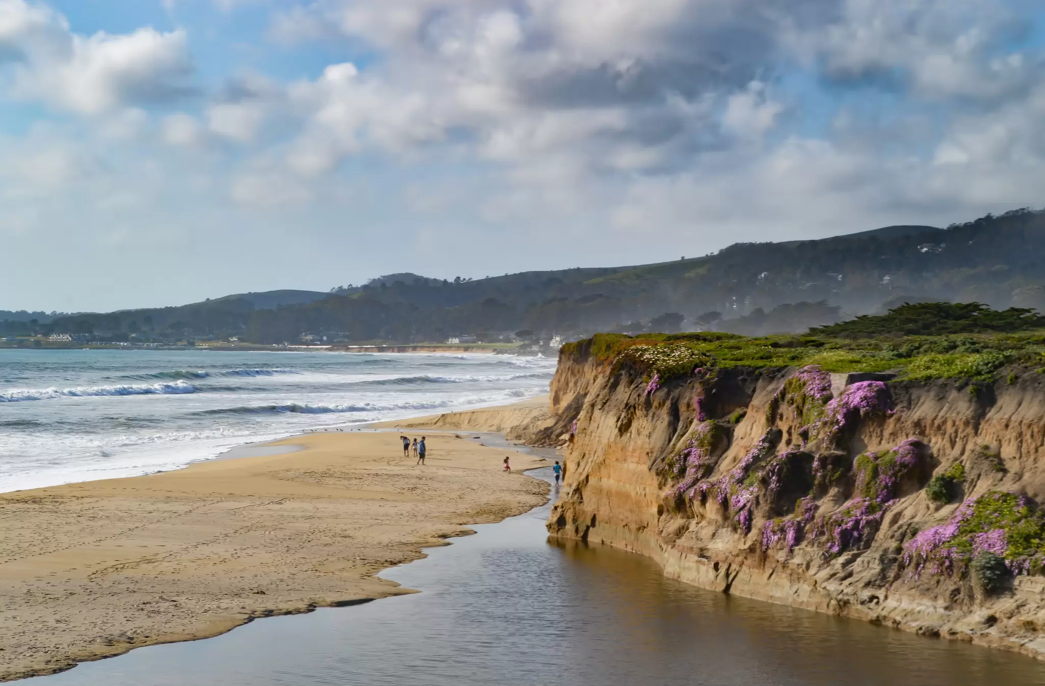 People on a sandy beach below a cliff.