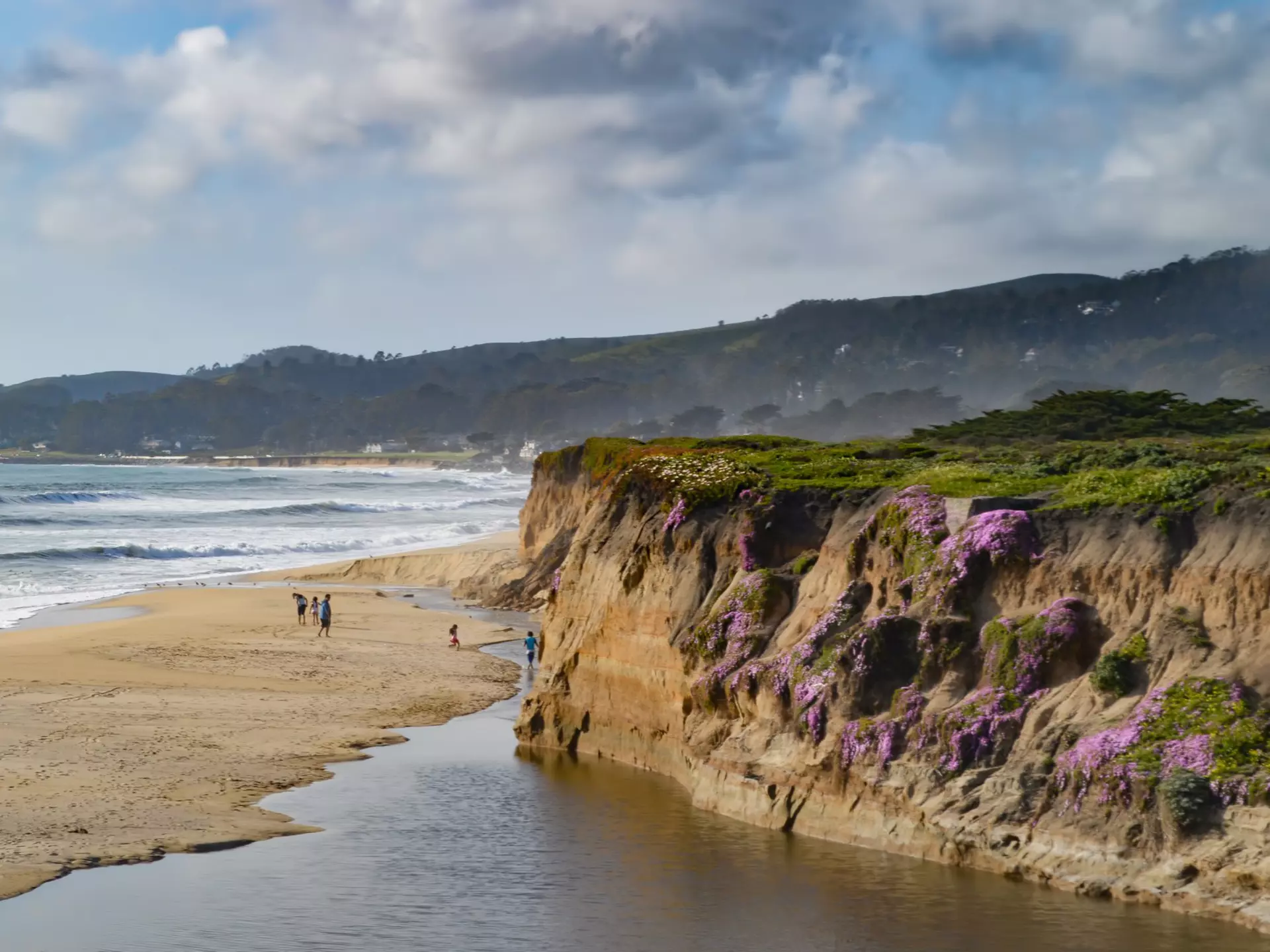 People on a sandy beach below a cliff.