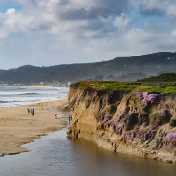 People on a sandy beach below a cliff.