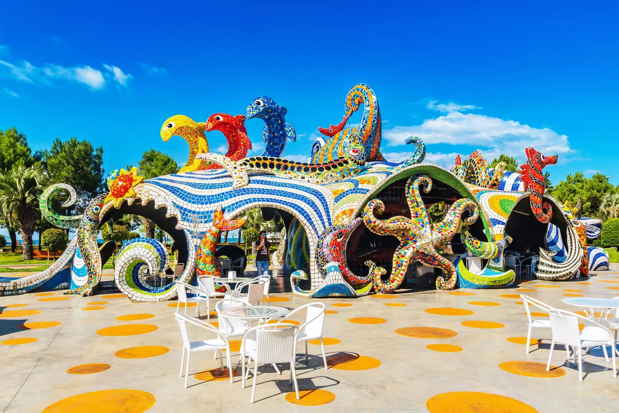 A curving structure on a seaside promenade that features starfish, fish, seahorses and other marine life all covered in colorful tiles.