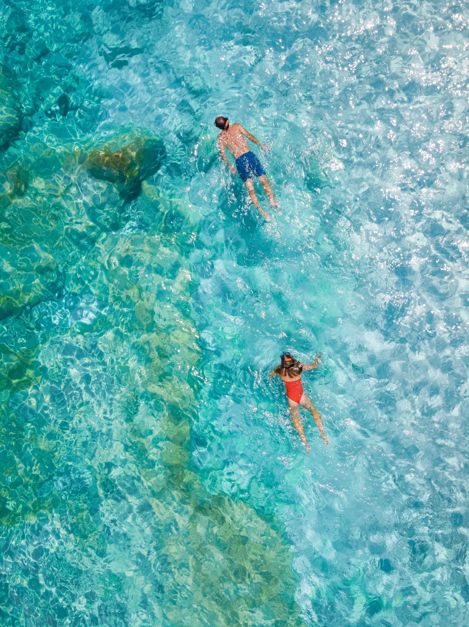 Snorkelers in clear shallow turquoise ocean swim near rocks