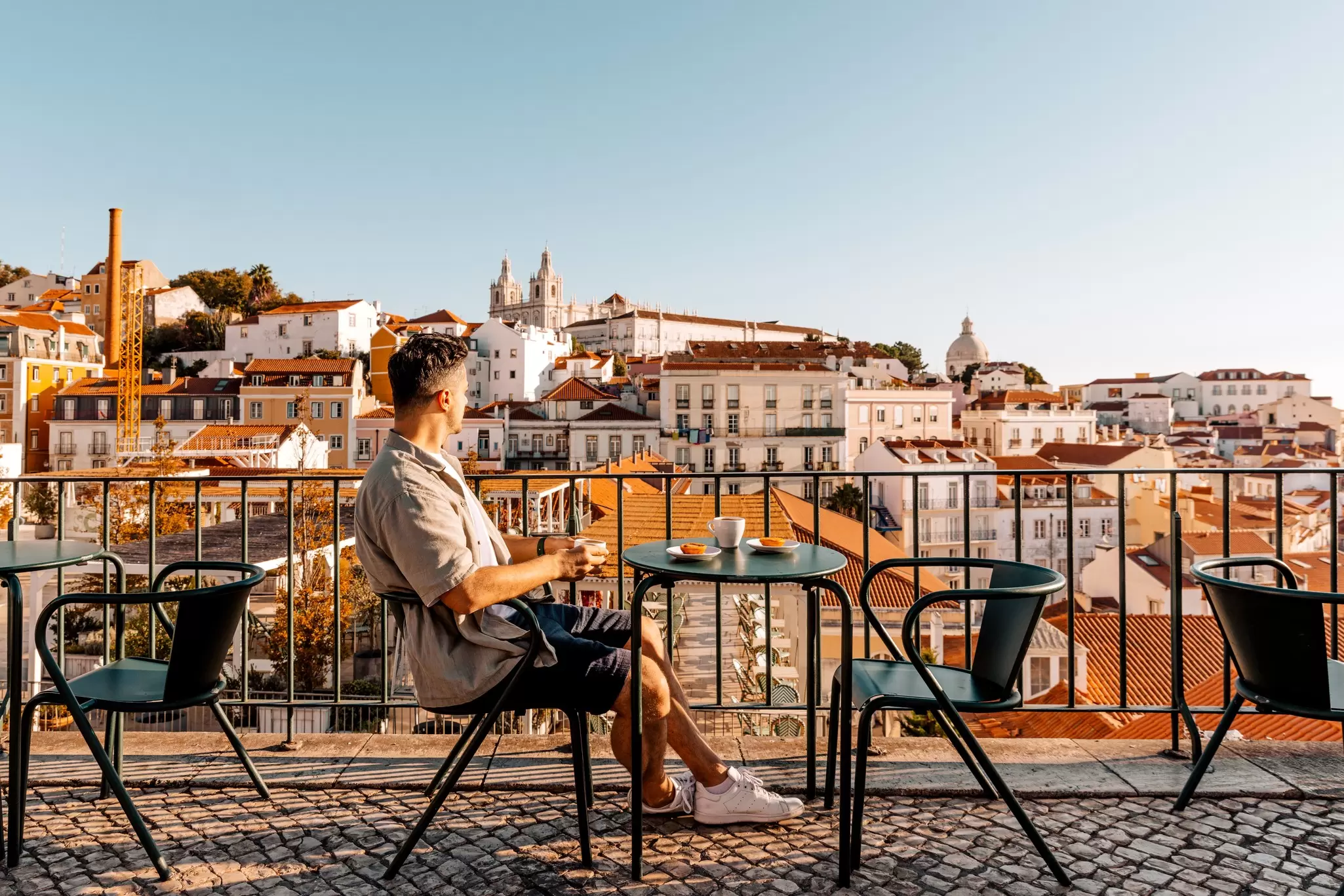Man sitting at a small table drinking coffee with a view of Lisbon, Portugal in the background
