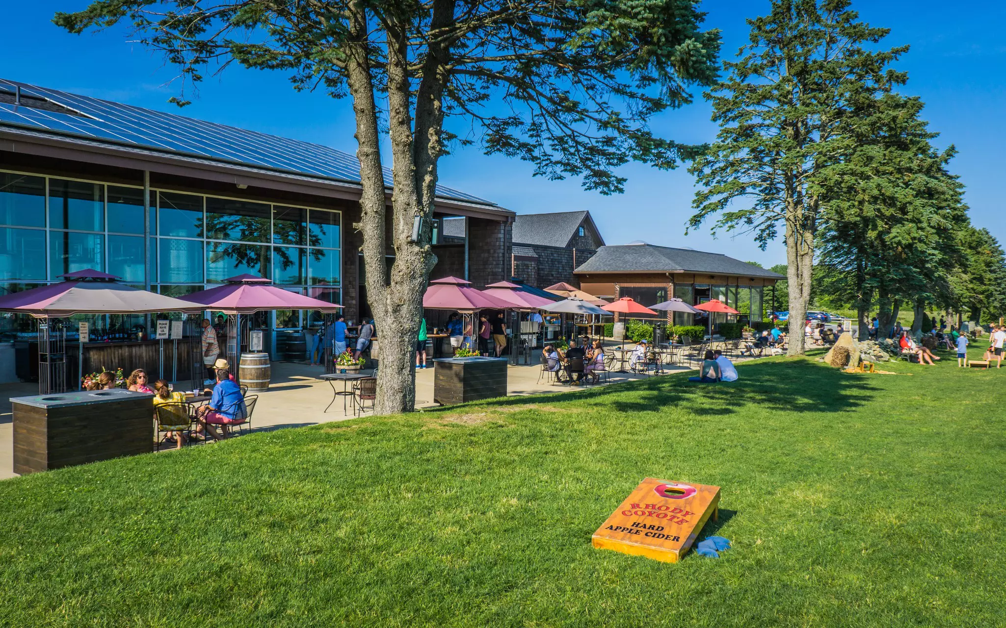 People at tables under umbrellas and on the lawn at a vineyard in Newport, Rhode Island.