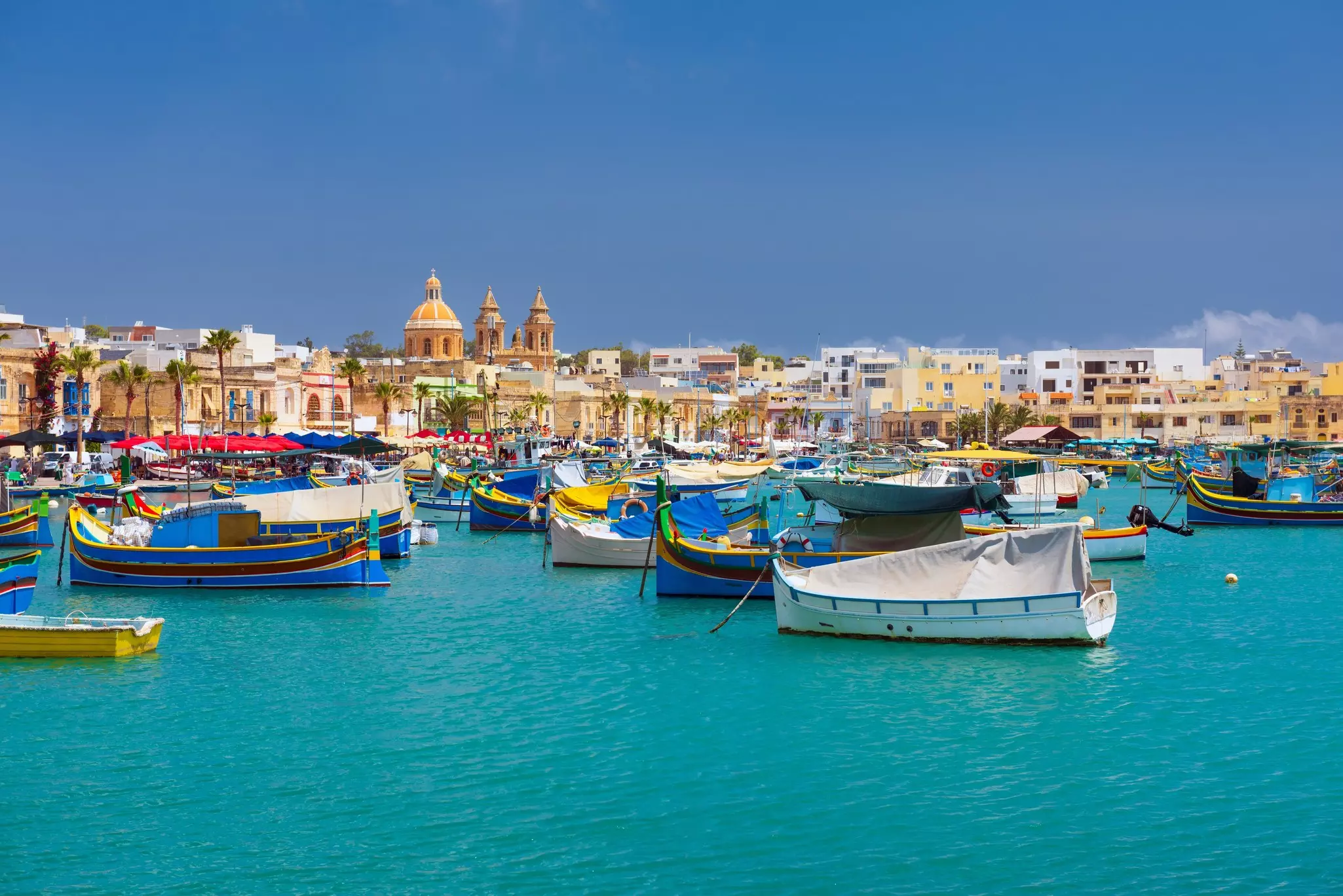 Colorful fishing boats fill a small town's harbor on a sunny day.