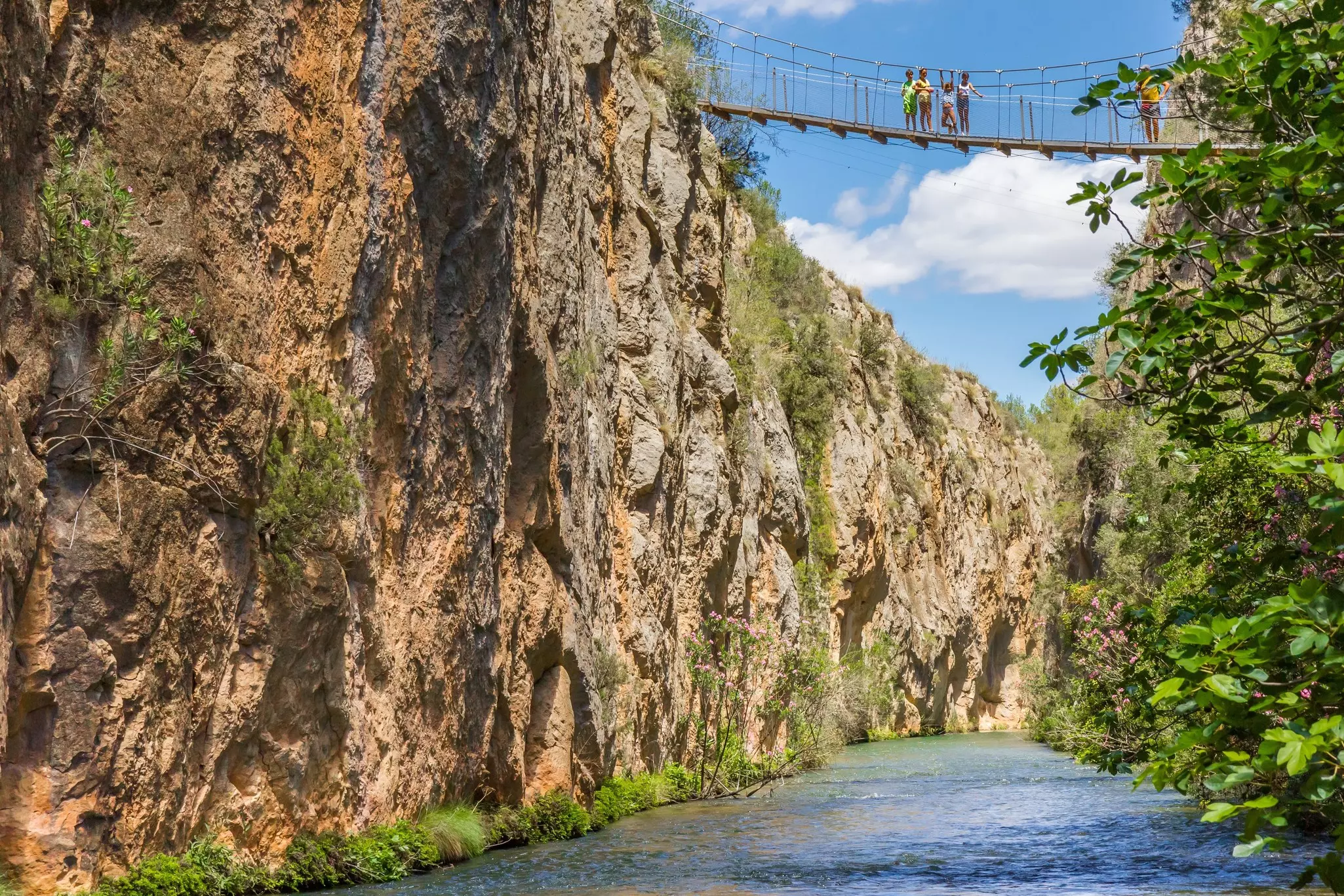 People on a suspension bridge over a river between two steep cliffs.