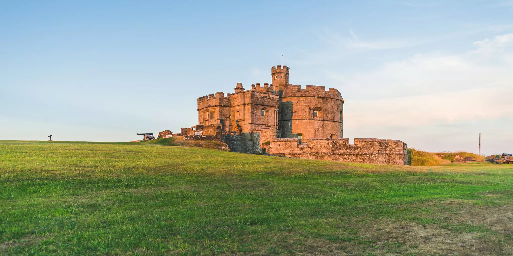 A semi-ruined castle on a grassy knoll is seen in the light of sunrise