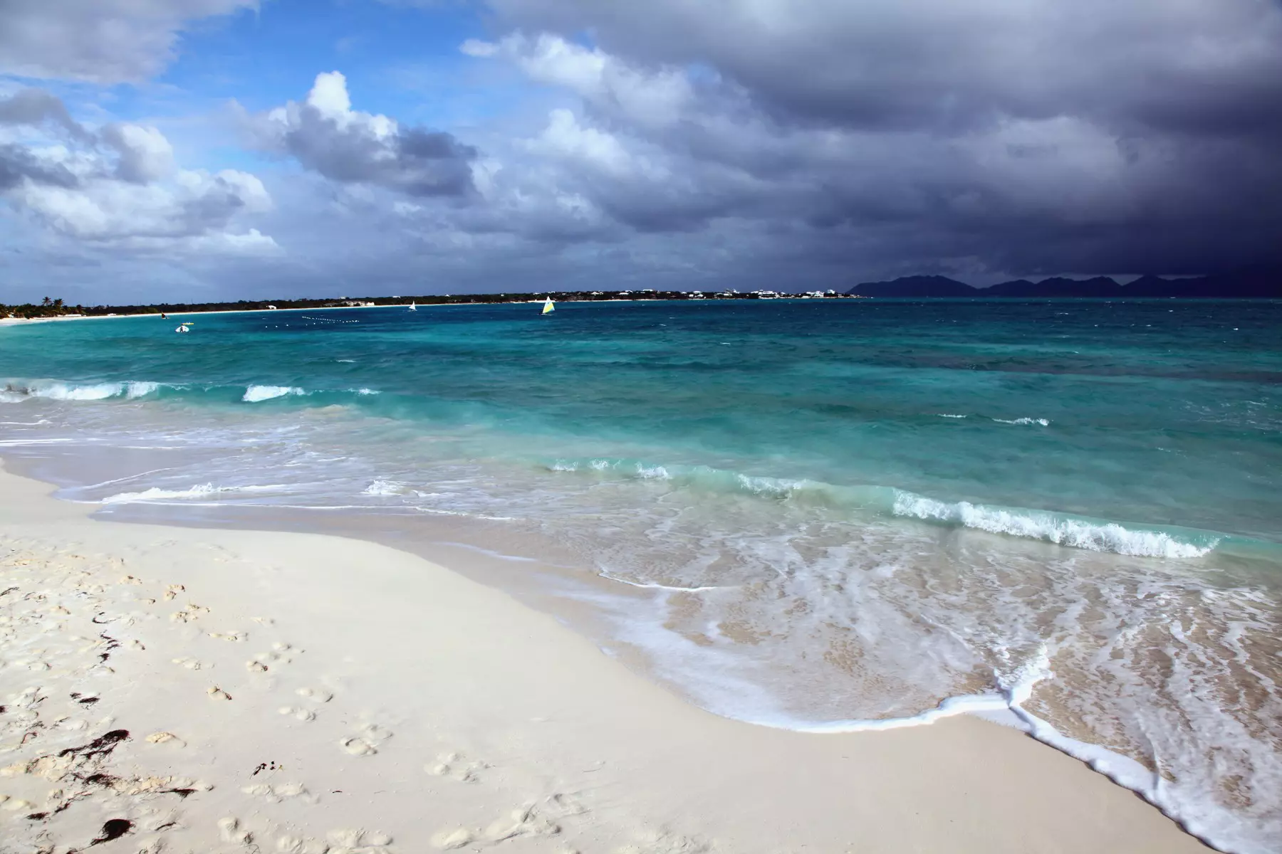 Dark clouds forming out to sea over an island with a sandy beach.