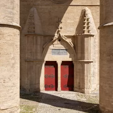 Red doors under a pointed Gothic arch between the two huge round stone pillars of the cathedral porch