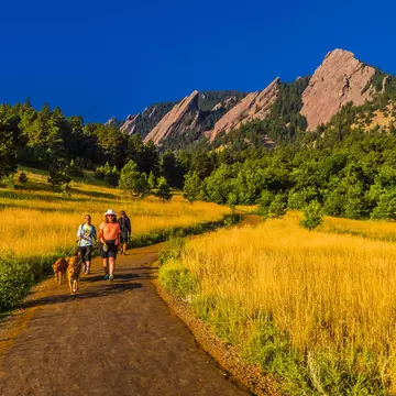 Hikers walking their dogs in front of the Flatirons rock formations
