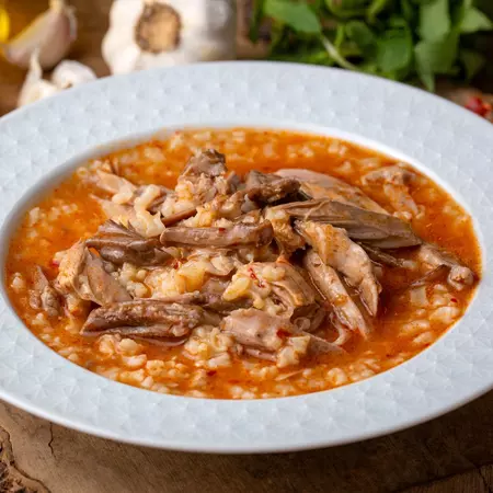 A white bowl full of a red soup with lamb meat. 