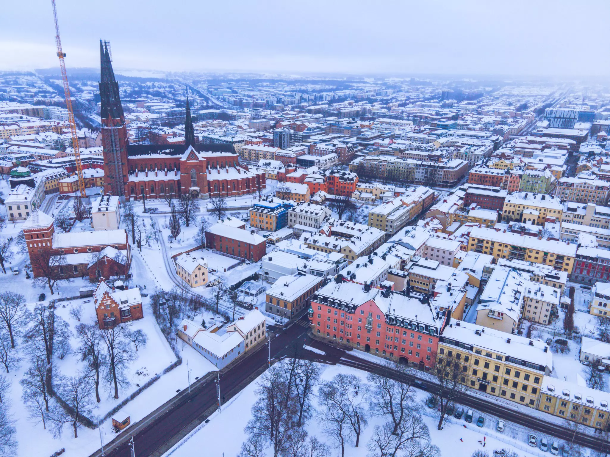 An aerial view of a city in winter, showing buildings and a large church covered with snow.
