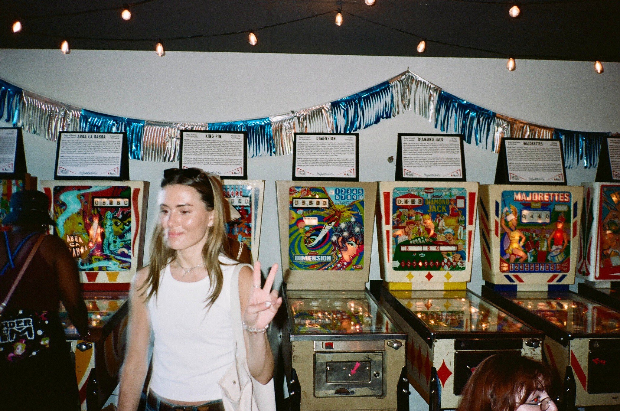 A person holds up a hand in an arcade with pinball machines.