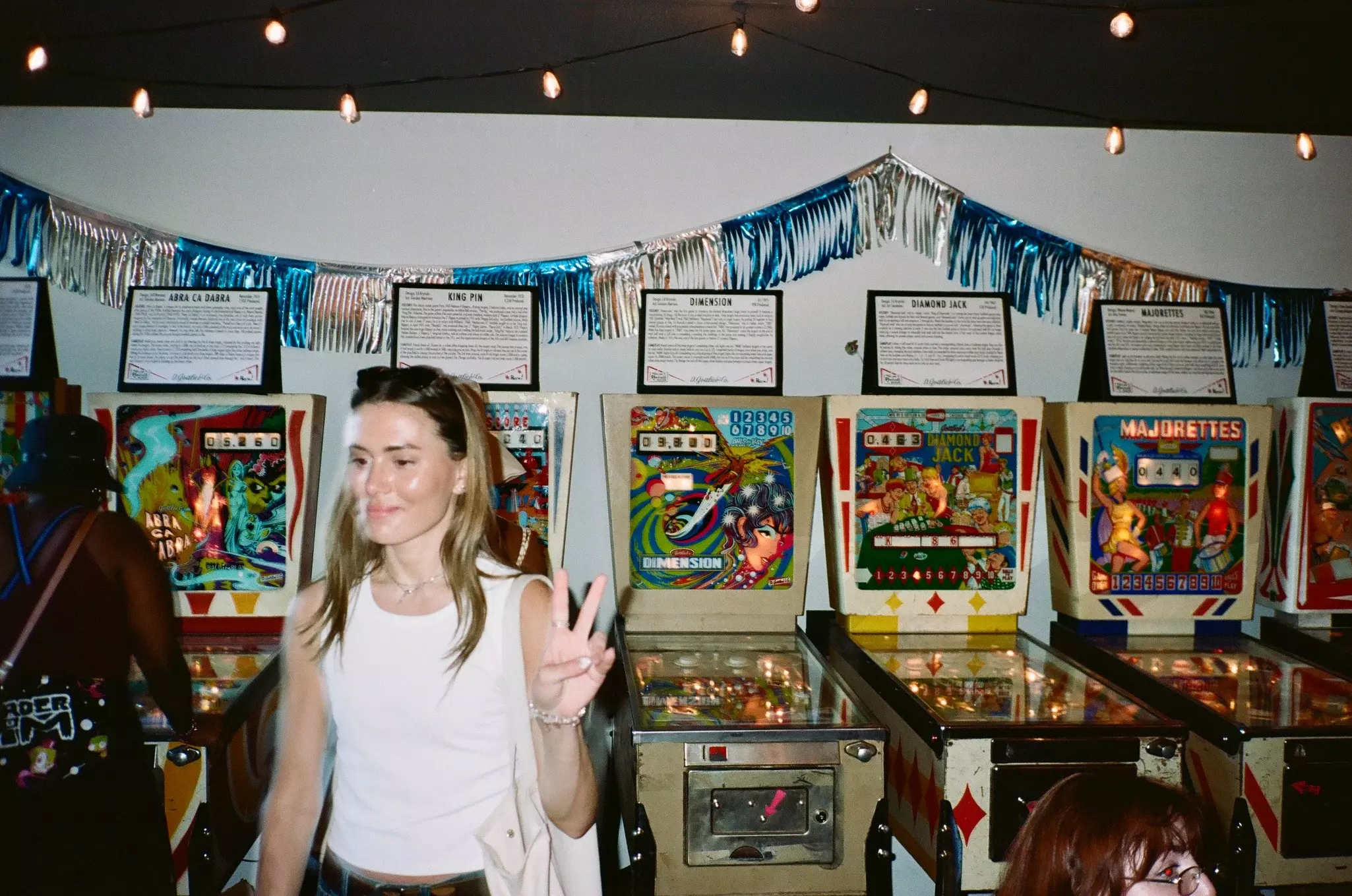 A person holds up a hand in an arcade with pinball machines.