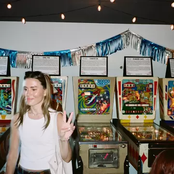 A person holds up a hand in an arcade with pinball machines.
