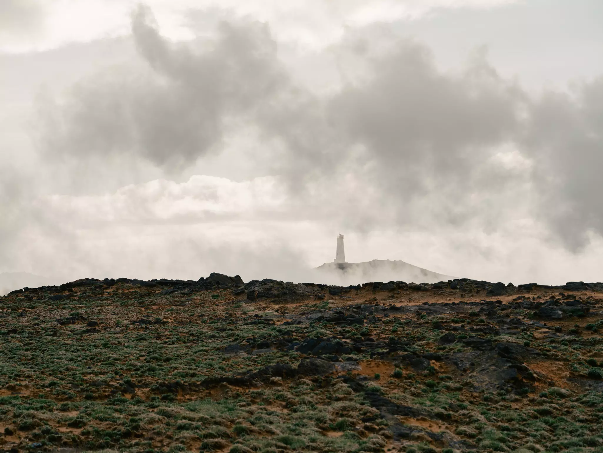 A mossy and rocky landscape with a lighthouse in clouds.