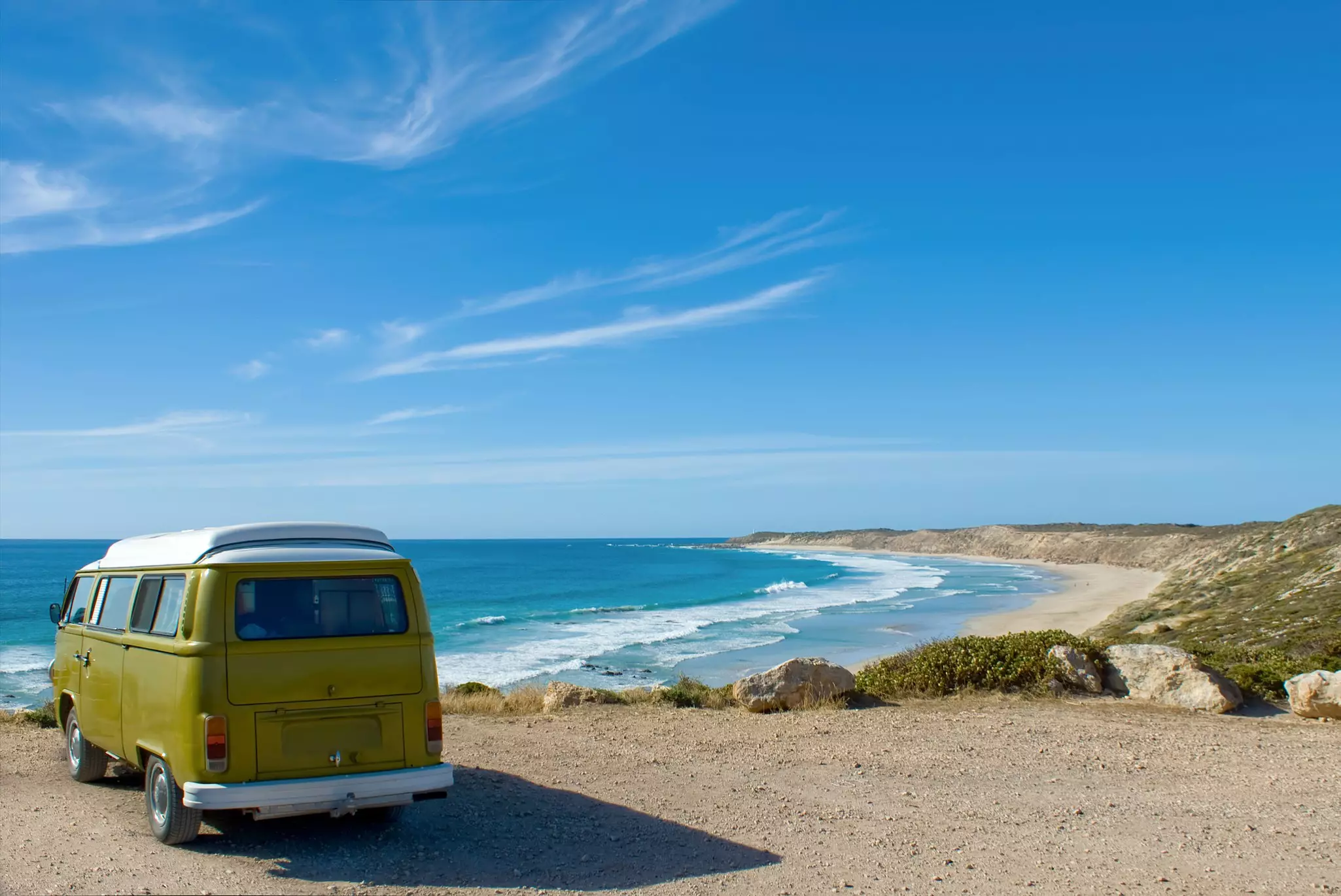 A small camper van parked at a viewpoint over a wide sandy beach.