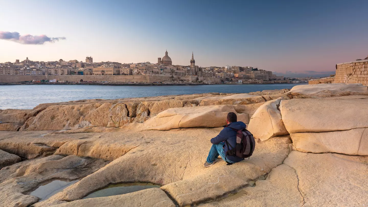 Man sitting on the rock and watch beautiful architecture of the Valletta city at dawn.
