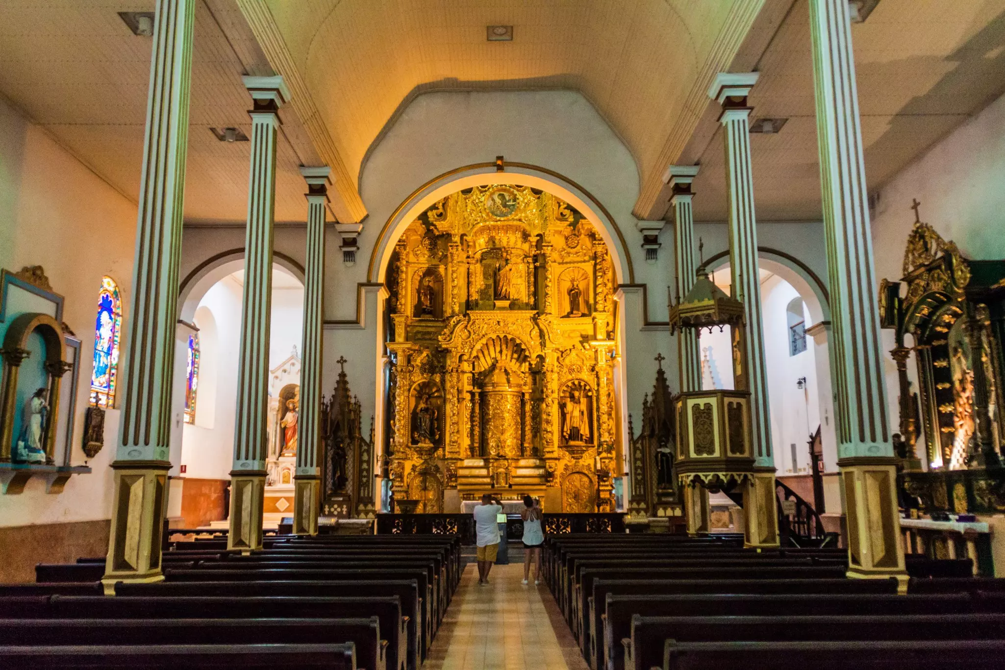 An ornate gilded altarpiece is seen in the interior of a church.