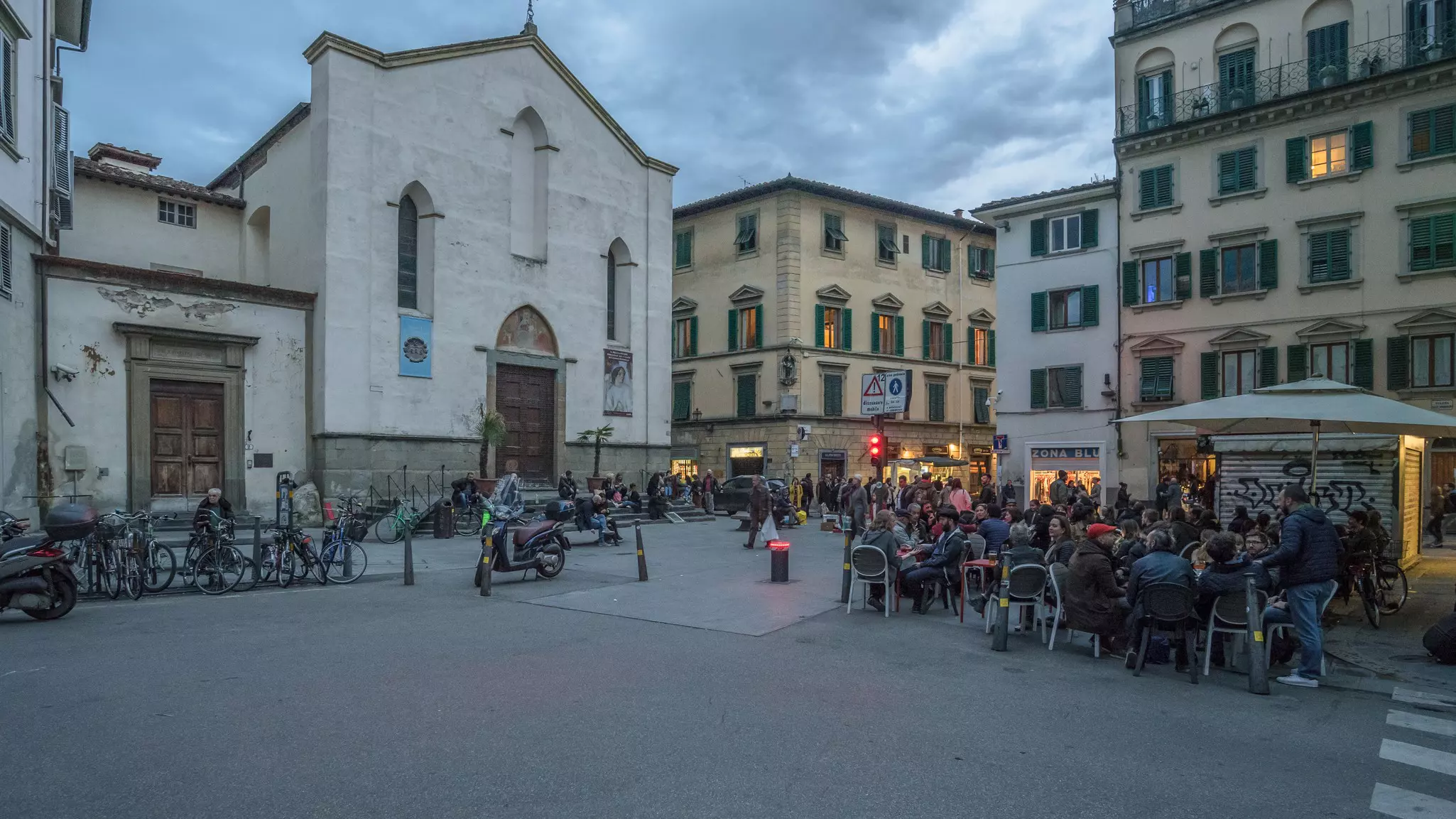 An open square with an outdoor cafe where people sit at tables after dusk.