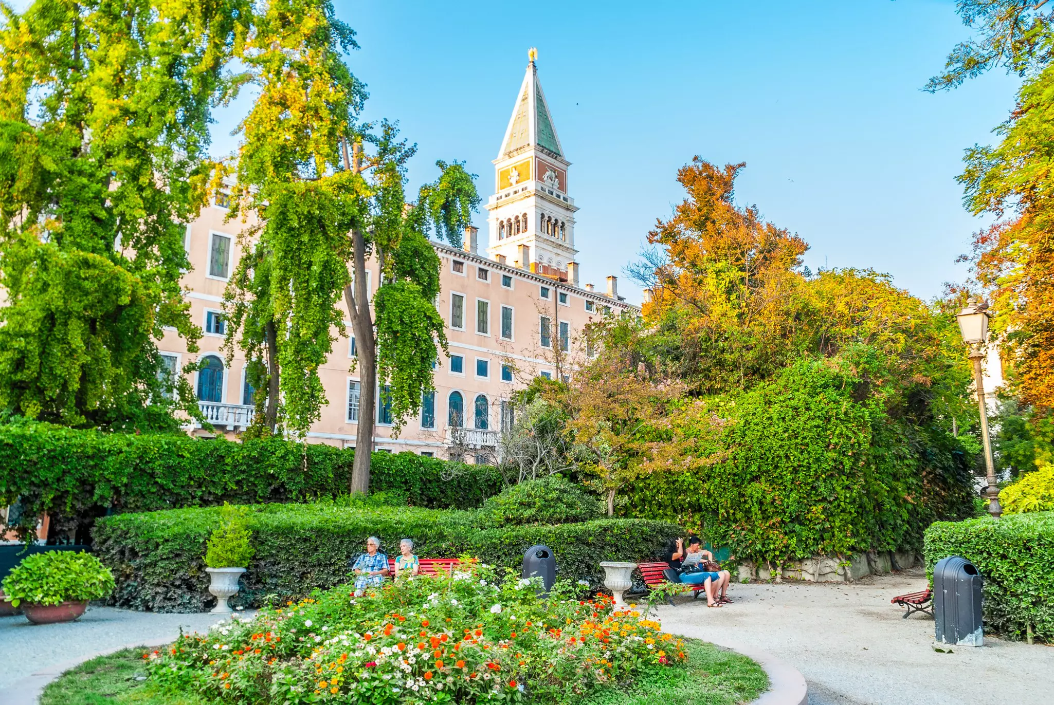 A green parkland overlooked by a tall pointed bell tower.
