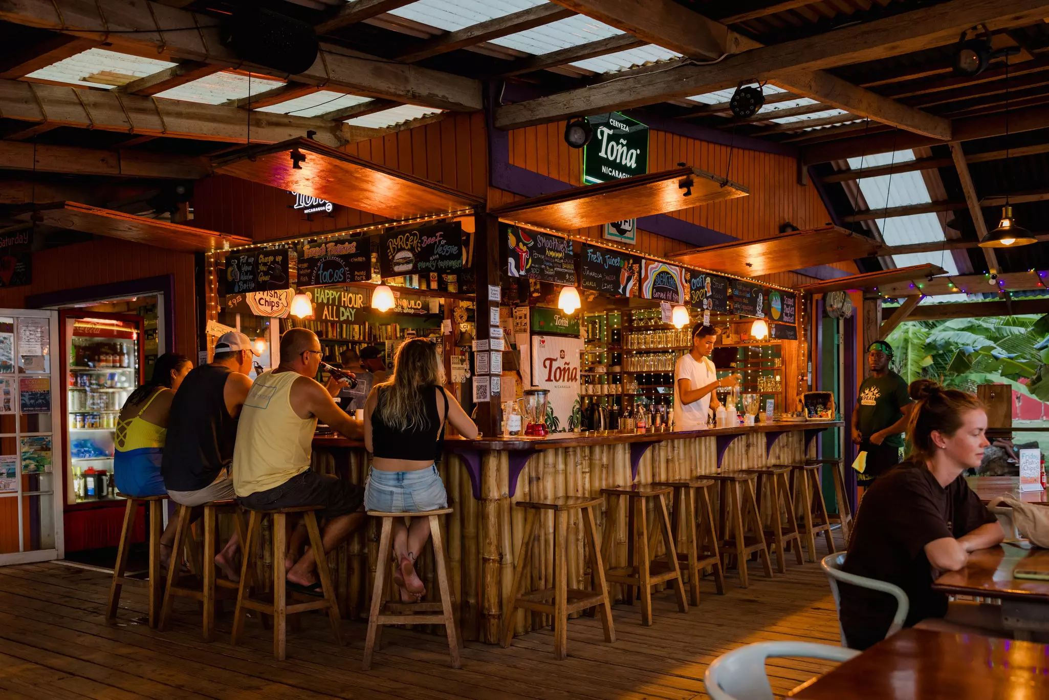 Four customers sit at barstools drinking beers in a small open-sided bar.