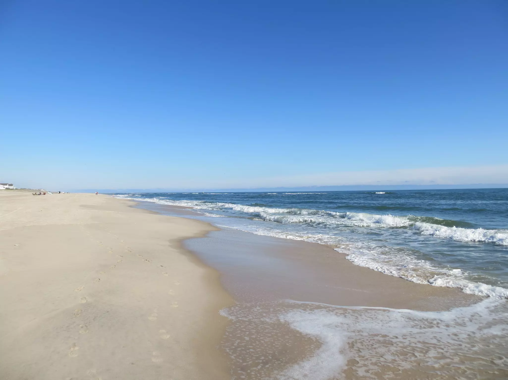 Wide sandy beach on a clear day with only a few people in the distance and the ocean to the right.
