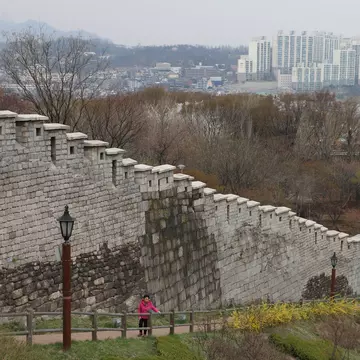 The old Seoul city walls with the skyline of Seoul in the distance, along a path in Naksan Park