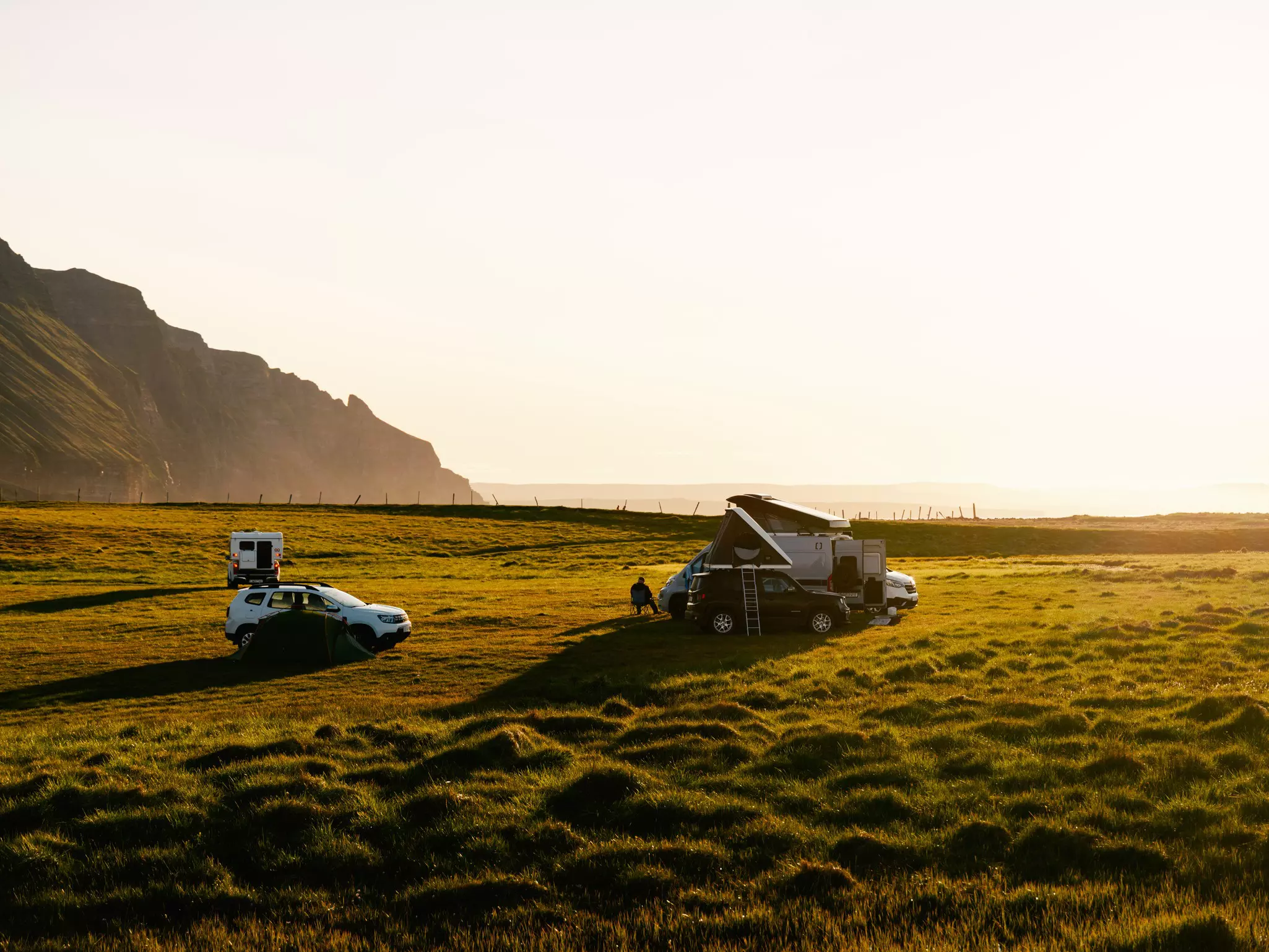 Three car camps on green turf with rocks and a beach in the background at sunset
