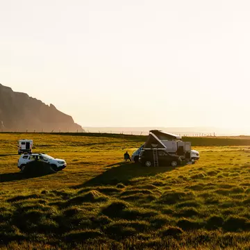 Three car camps on green turf with rocks and a beach in the background at sunset
