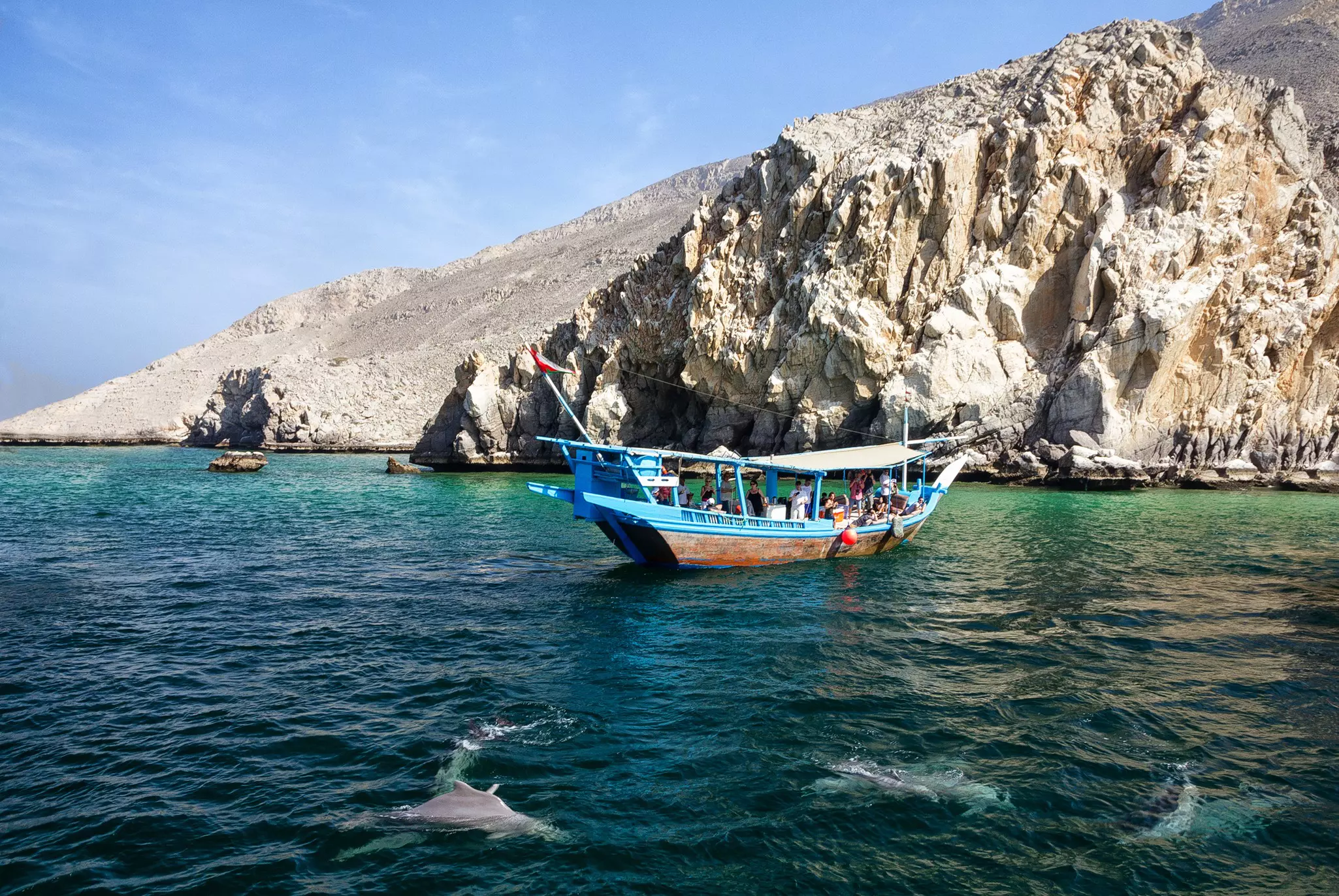 Khasab, Oman - June 22, 2019: Dolphins and tourist dhow boat in fjords.