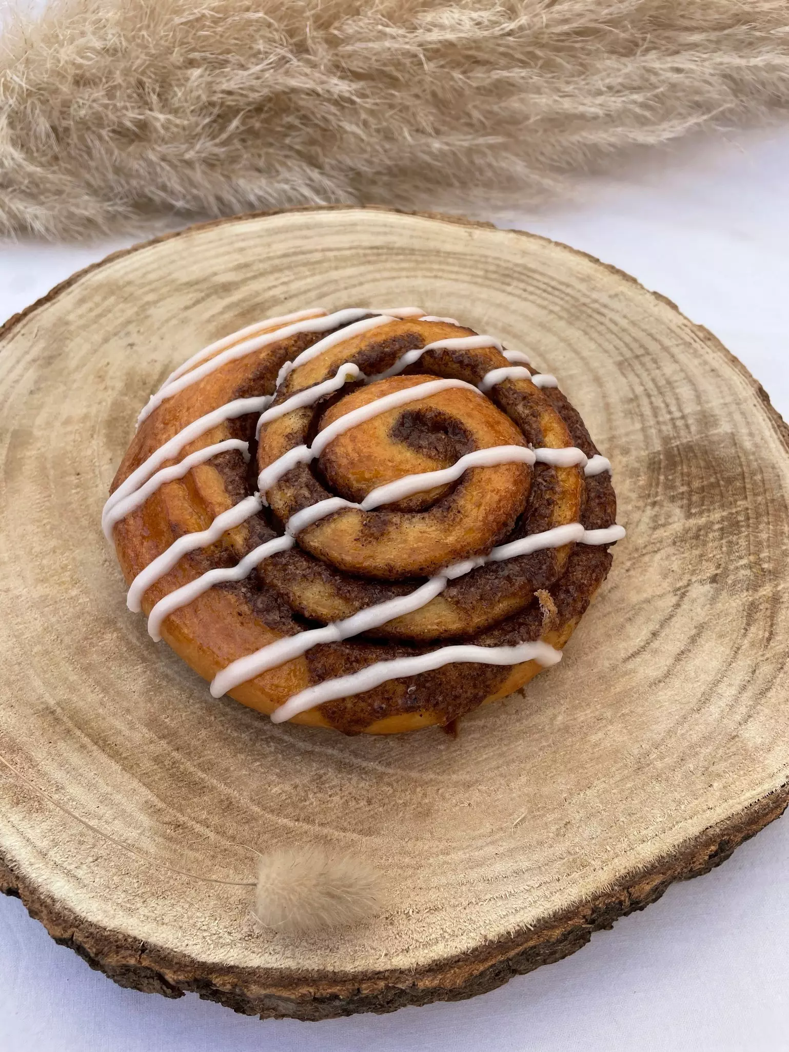 A swirled cinnamon pastry with stripes of icing on a round wooden platter.