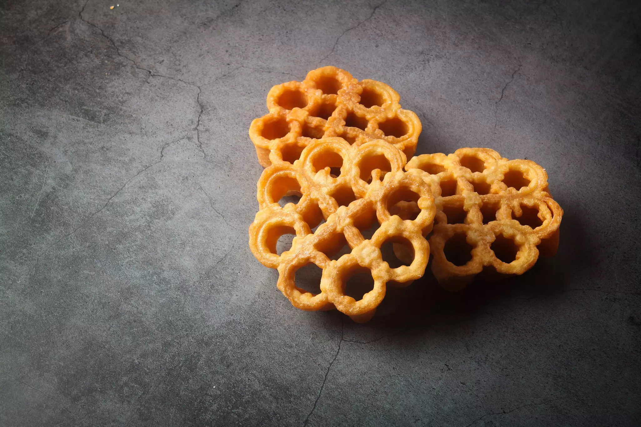 Three traditional Christmas cookies known as rose cookies in a pile on a grey board