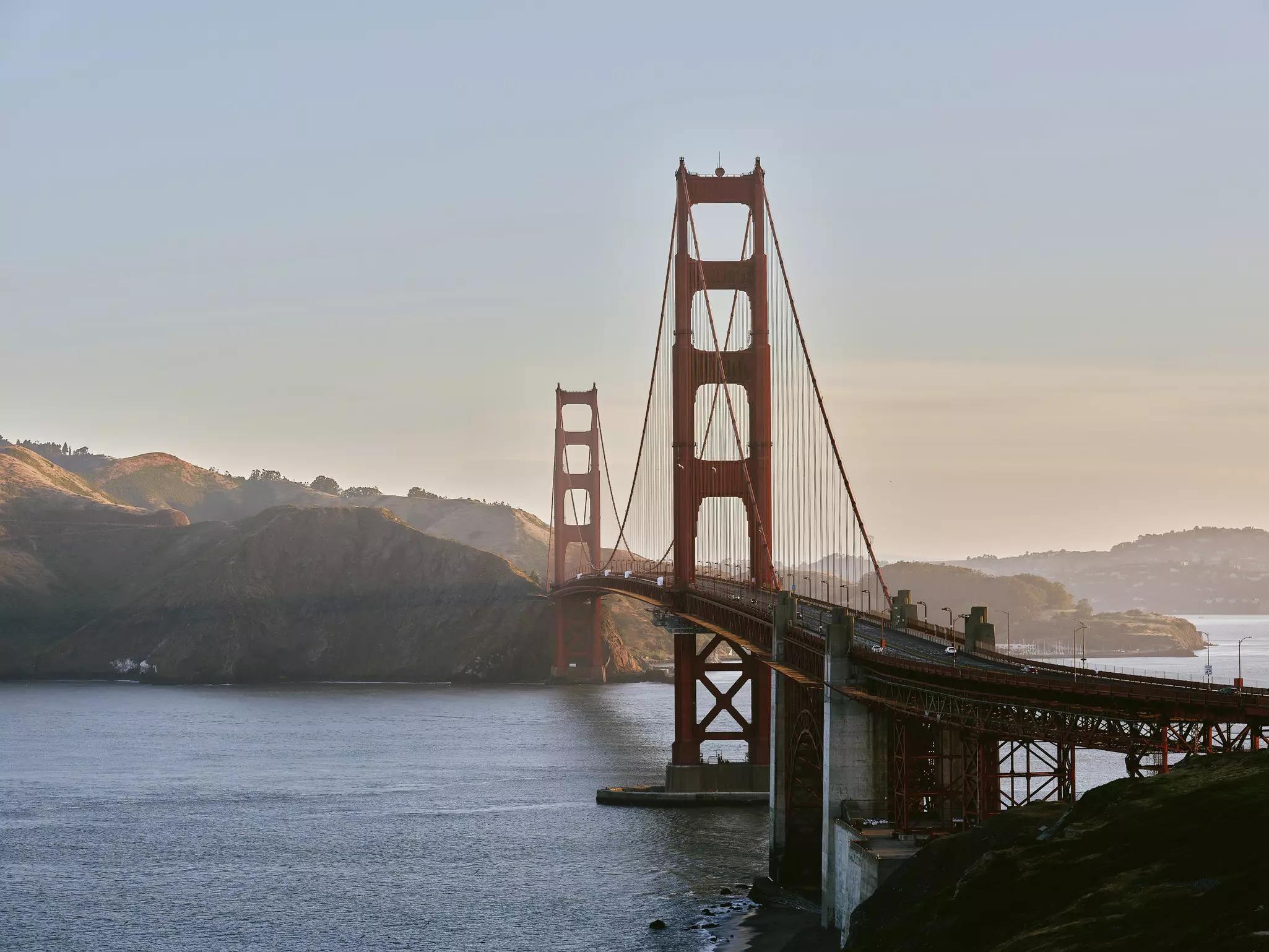 A large orange steel suspension road bridge over a waterway.