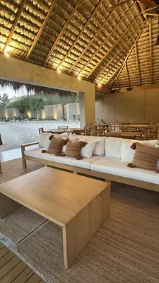 Brown, luxury tent near water at sunset. Palm trees surround it. 