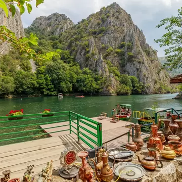 Copper teapots on a ledge above a boat jetty on the green lake of Matka Canyon near Skopje, North Macedonia