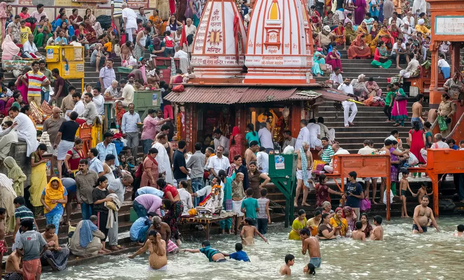 Pilgrims bathe in the Ganges at a Haridwar ghat, crowds on the steps around a red-and-white Hindu shrine