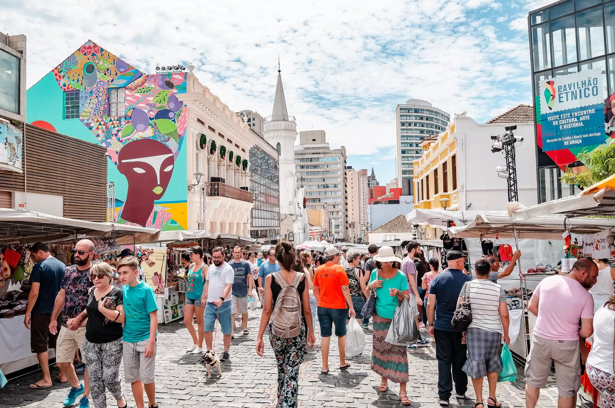 Crowds of people wander down a cobbled street in a city market