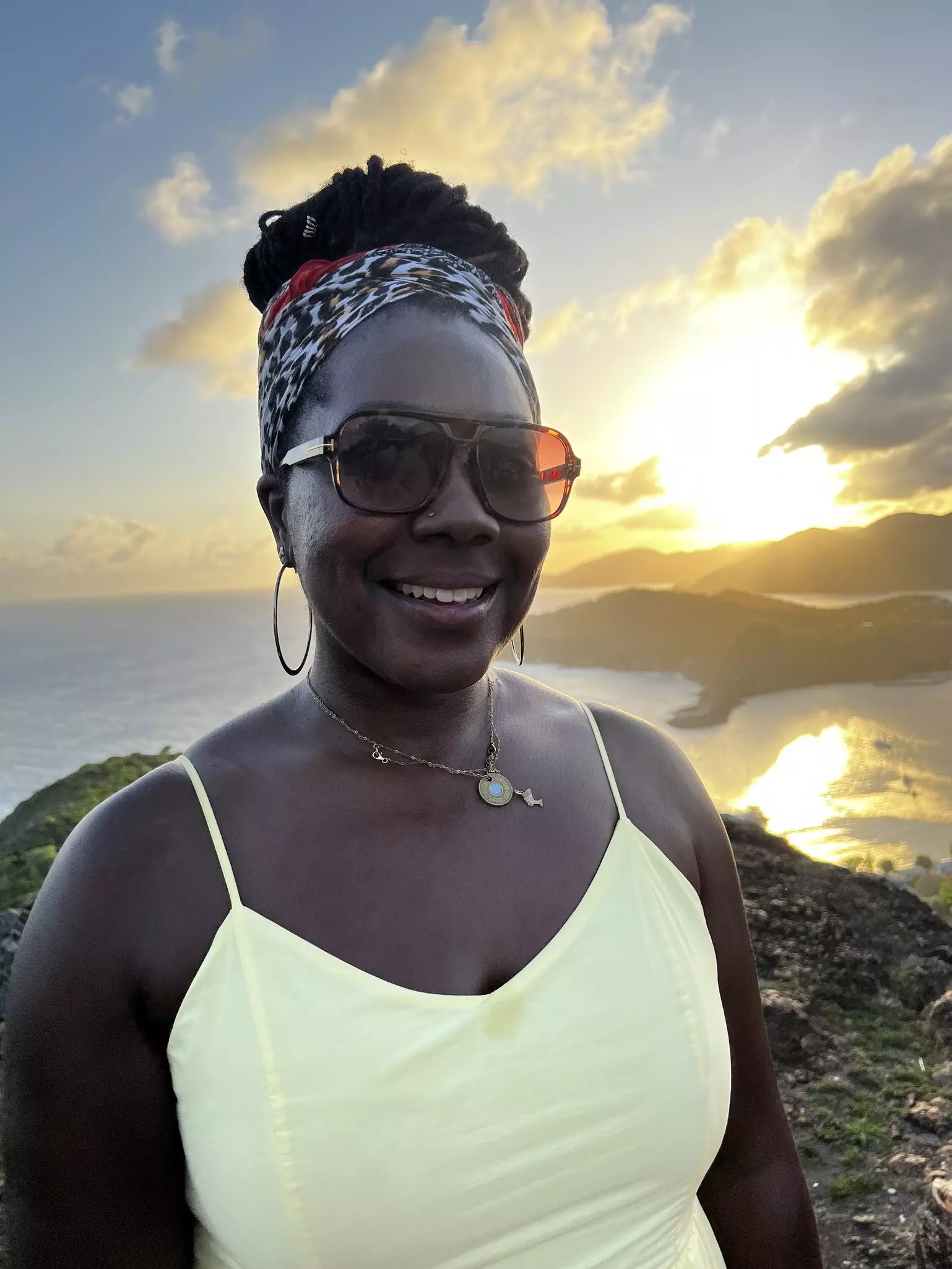 Destination Editor Alicia Johnson, wearing a yellow dress, poses for the camera at a viewpoint as the sun sets behind her.