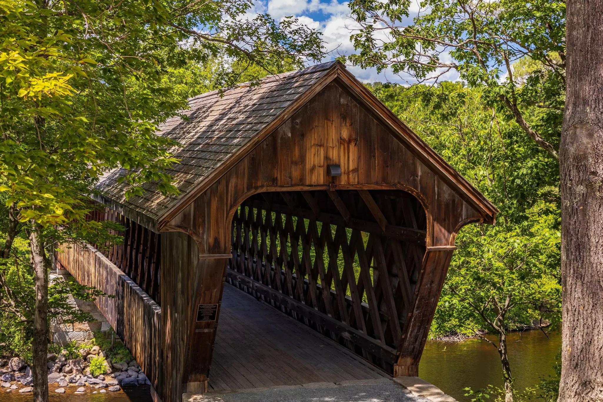 A wooden covered bridge over a stream is pictured in summer.